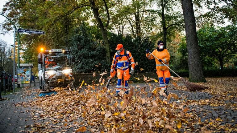 Businessfotografie - Männer fegen das Herbstlaub zusammen